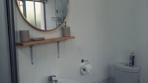 A bathroom with a white sink, a toilet, a mirror, and a shelf with toiletries.