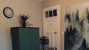 A bedroom with a bed, a green wardrobe, a radiator, a fan, a clock, and a forest mural on the wall.