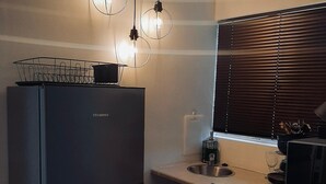 A compact kitchen with a refrigerator, a sink, and a window with blinds.