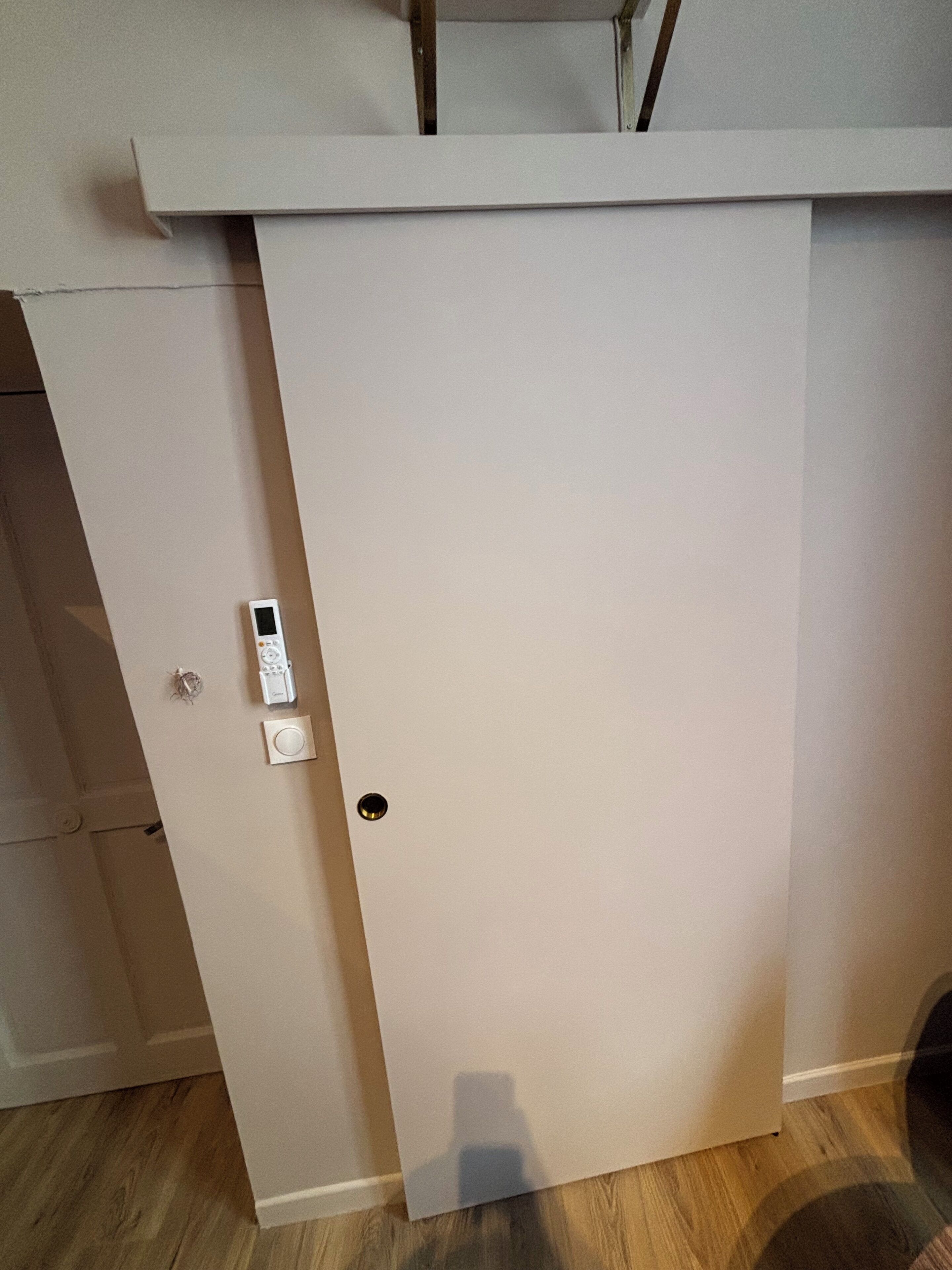 A closed door with a keypad lock and a small hole, possibly for a peephole, in a room with wooden flooring.