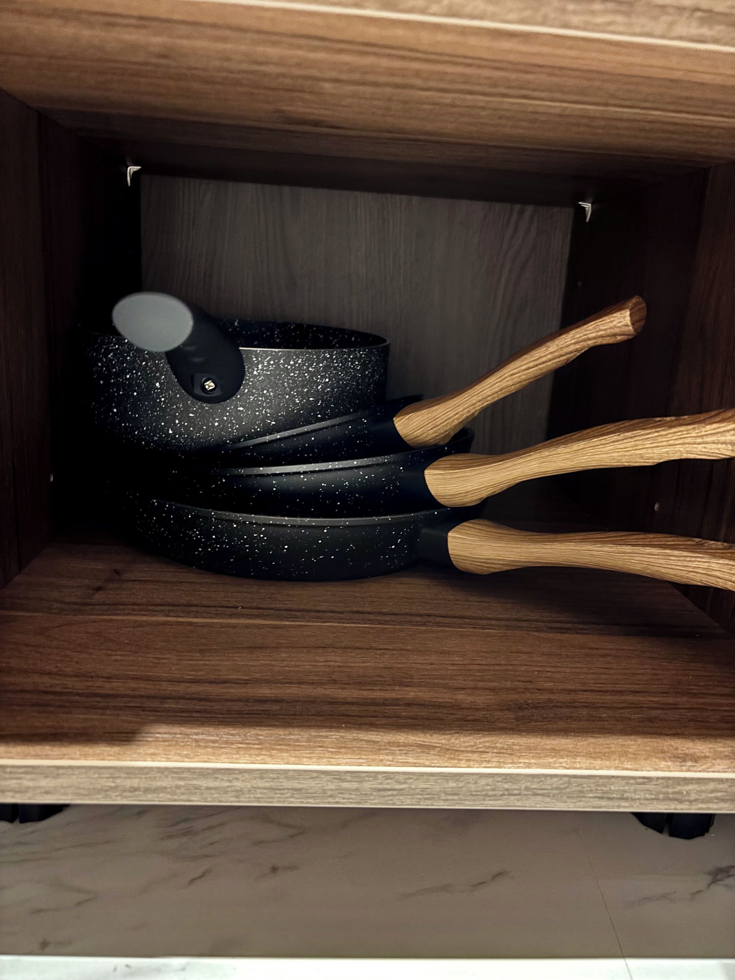 Ein Holzkabinett mit einer schwarzen, gefleckten Bratpfanne und drei Spateln mit Holzgriffen.