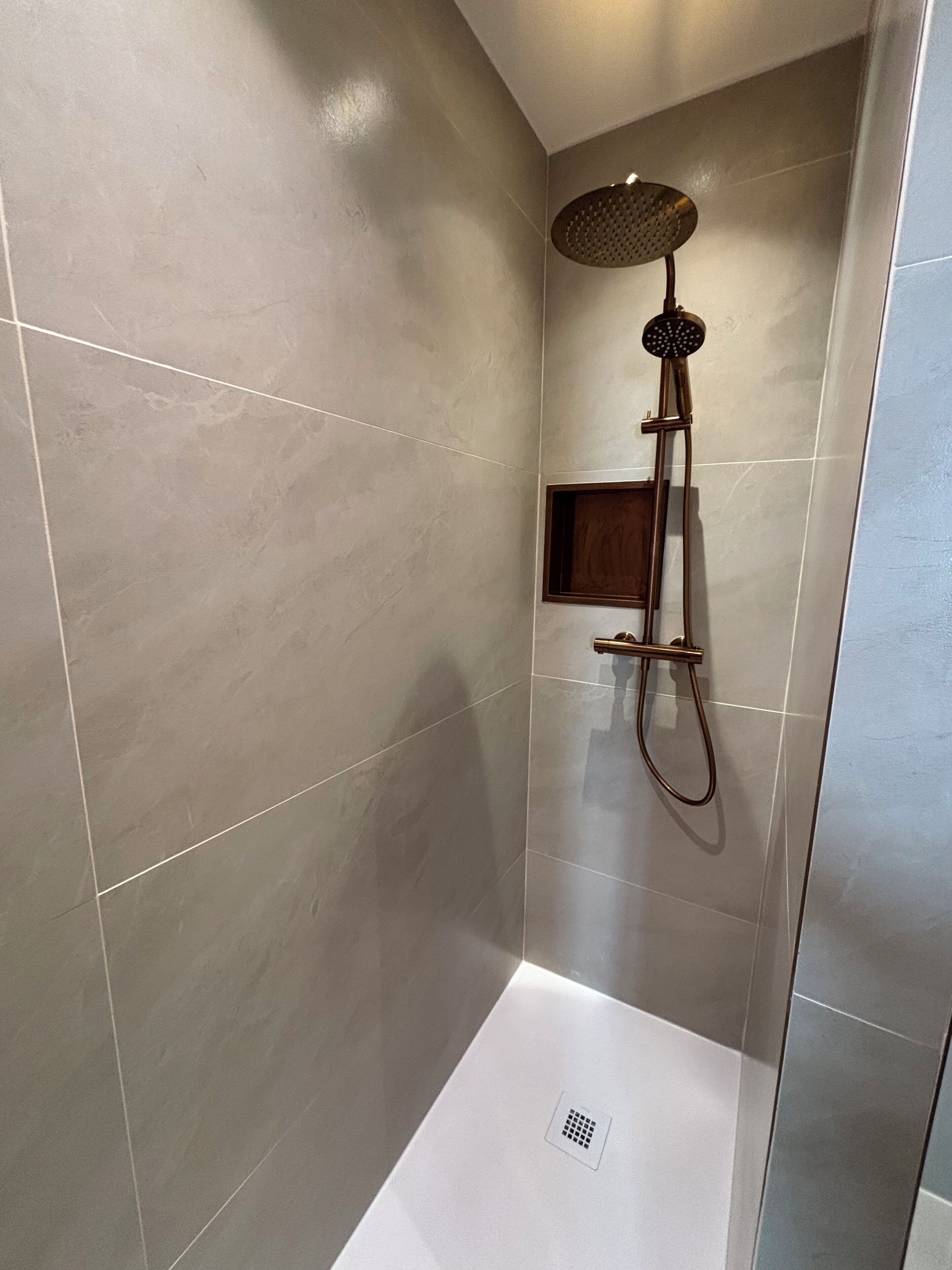 Een moderne douche met een handdouche en een bedieningspaneel aan de muur.