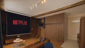 Ein gemütliches Wohnzimmer mit einem großen Fernseher, der das Netflix-Logo zeigt, einer Holztreppe und einer bequemen Sitzgelegenheit.