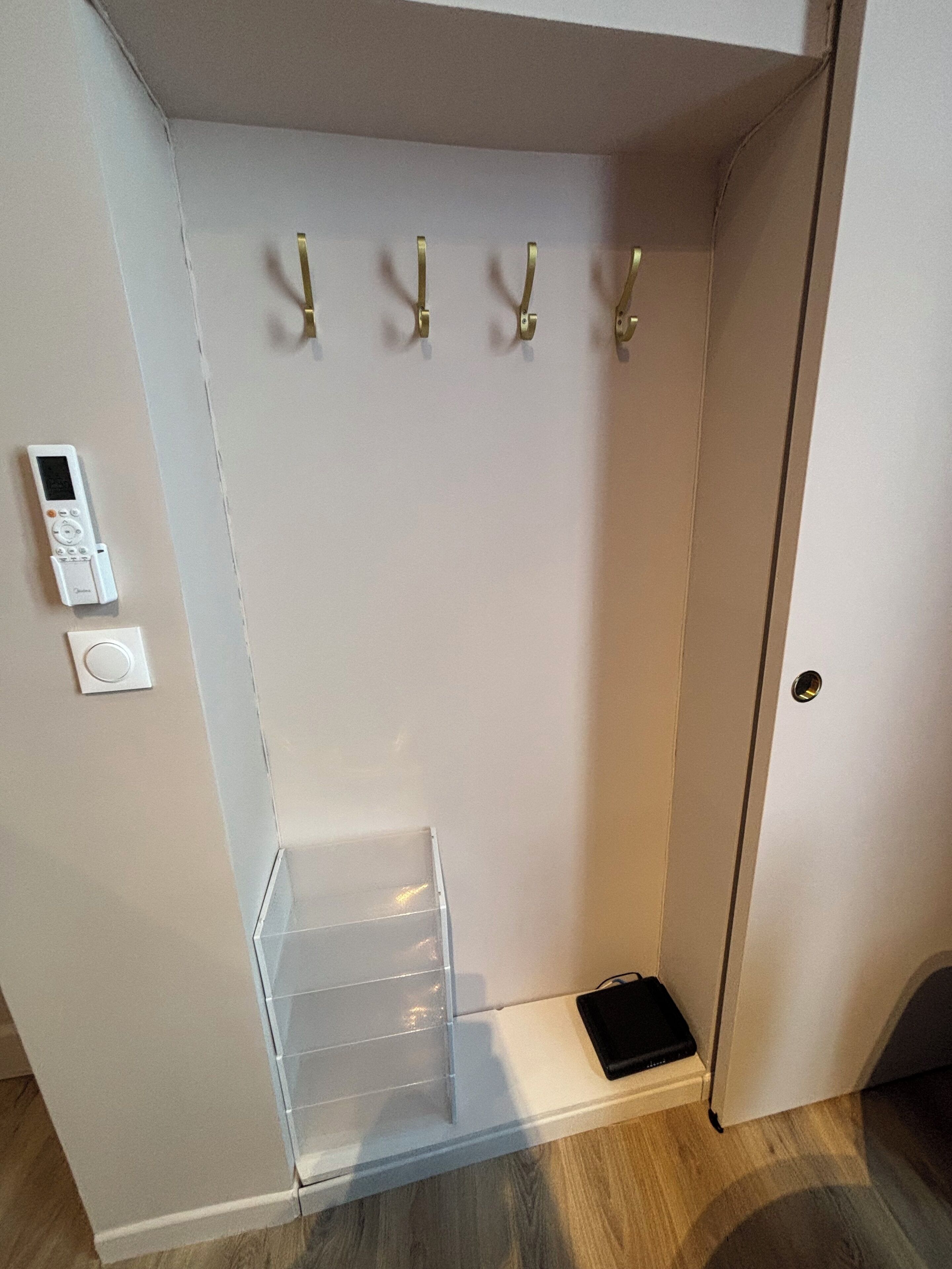 A small, enclosed closet with a built-in shelf, a hanging rod, and a thermostat on the wall.