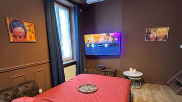 A hotel room with a large bed, a television mounted on the wall, and a small round table with candles.