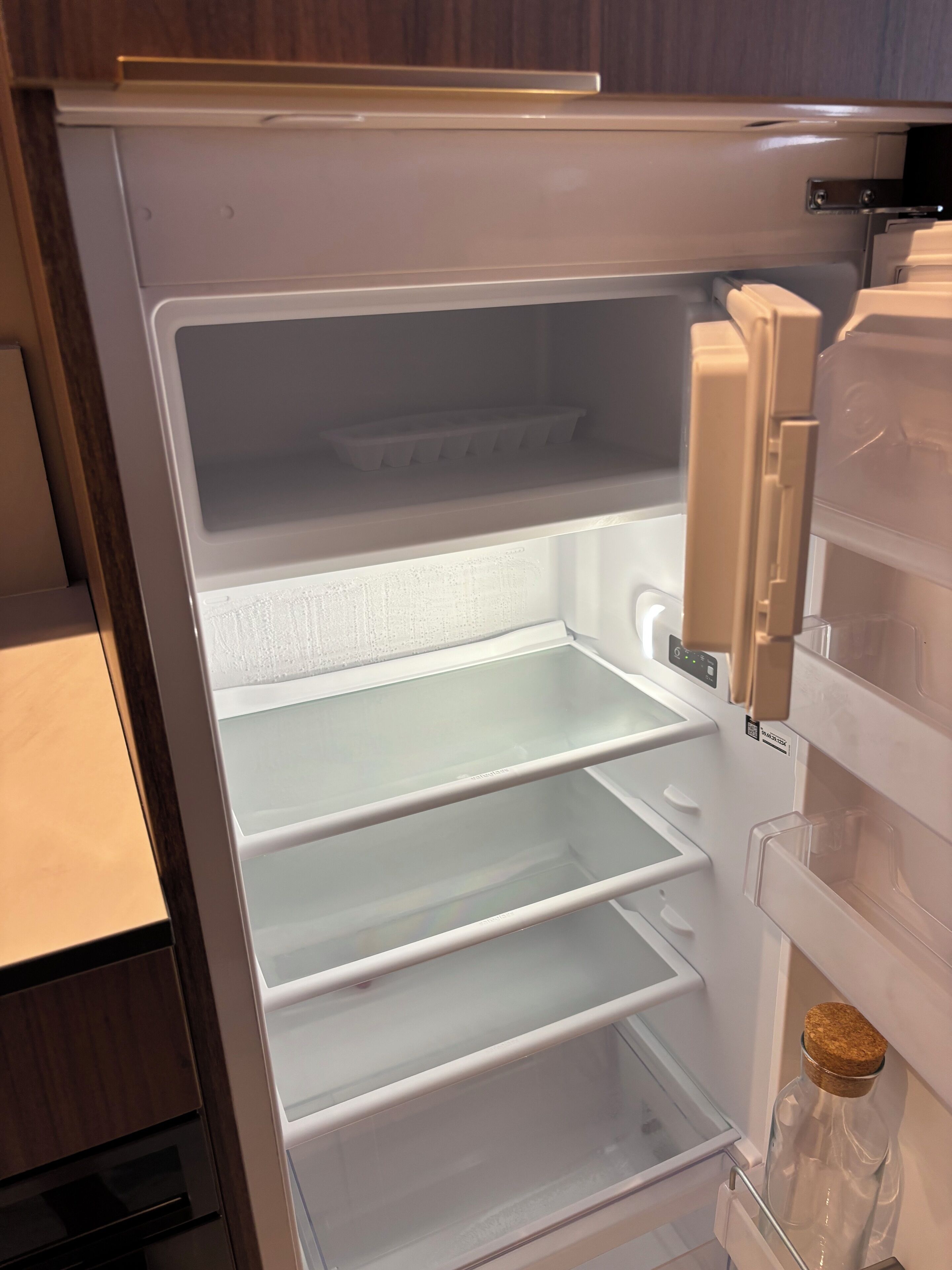 Un refrigerador abierto con varias estantes y una botella de vino en la puerta.