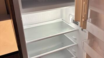 Un refrigerador abierto con varias estantes y una botella de vino en la puerta.