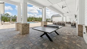 An outdoor patio area with a ping pong table, seating, and a view of a swimming pool. - Landing | Amazing 1BD, Gym, Clubhouse (Fort Myers)