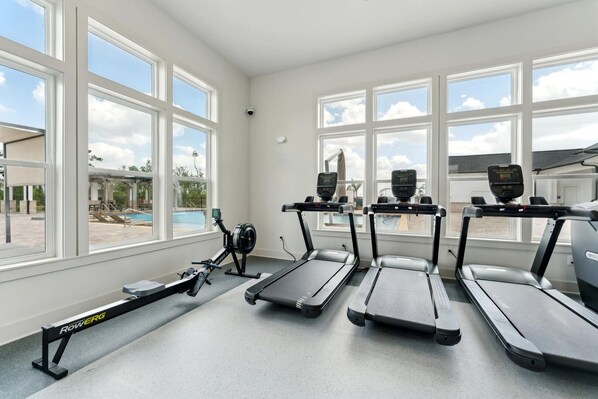 A gym with treadmills, a rowing machine, and a stationary bike, with large windows overlooking a swimming pool. - Landing | Stunning 1BD, Pool, Gym (Fort Myers)