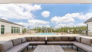 A poolside area with a large sectional sofa, a wooden table, and a view of a swimming pool and surrounding greenery. - Landing | Amazing 1BD, Pool, Clubhouse (Fort Myers)