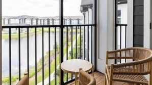 Un balcon donnant sur une rivière et des immeubles, aménagé avec des fauteuils en osier et une petite table ronde.