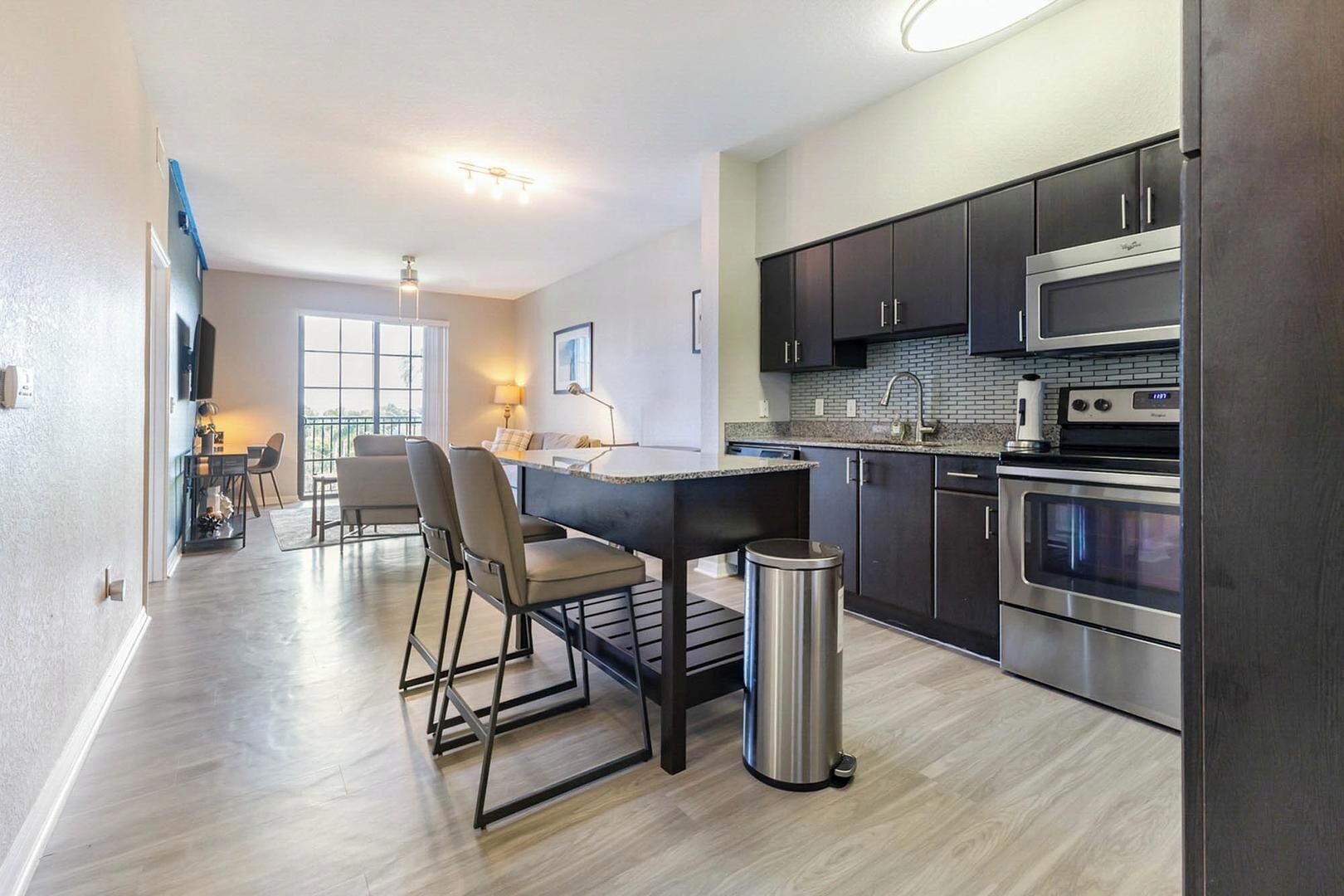 A modern kitchen with dark cabinets, stainless steel appliances, and a dining area with a table and chairs.
