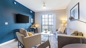 A modern living room with a blue accent wall, a flat-screen TV, a dining area, and a balcony with a view.