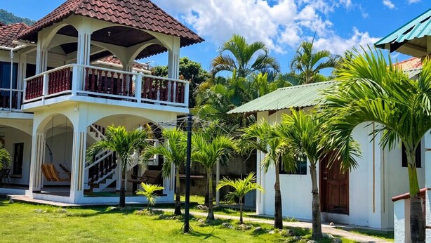 Un bâtiment à deux étages doté d’un balcon, entouré d’une pelouse bien entretenue et de palmiers.