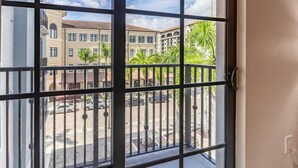 A view from a balcony with a metal railing, overlooking a street with parked cars and buildings with a tiled roof. - Landing | Modern 1BD, Gym, Clubhouse (Miramar)