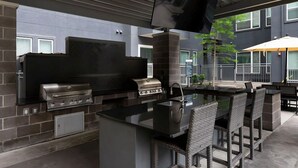 An outdoor kitchen with a grill, a TV mounted on a wall, and outdoor seating.