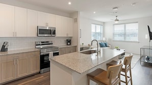 A modern kitchen with white cabinets, stainless steel appliances, a granite countertop, and a central island with bar stools. - Landing | Spectacular 1BD, Gym, Clubhouse (Rockwall)
