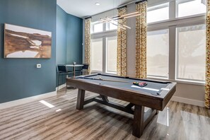 Een biljarttafel in een kamer met een blauwe muur, een schilderij en een raam met gordijnen.