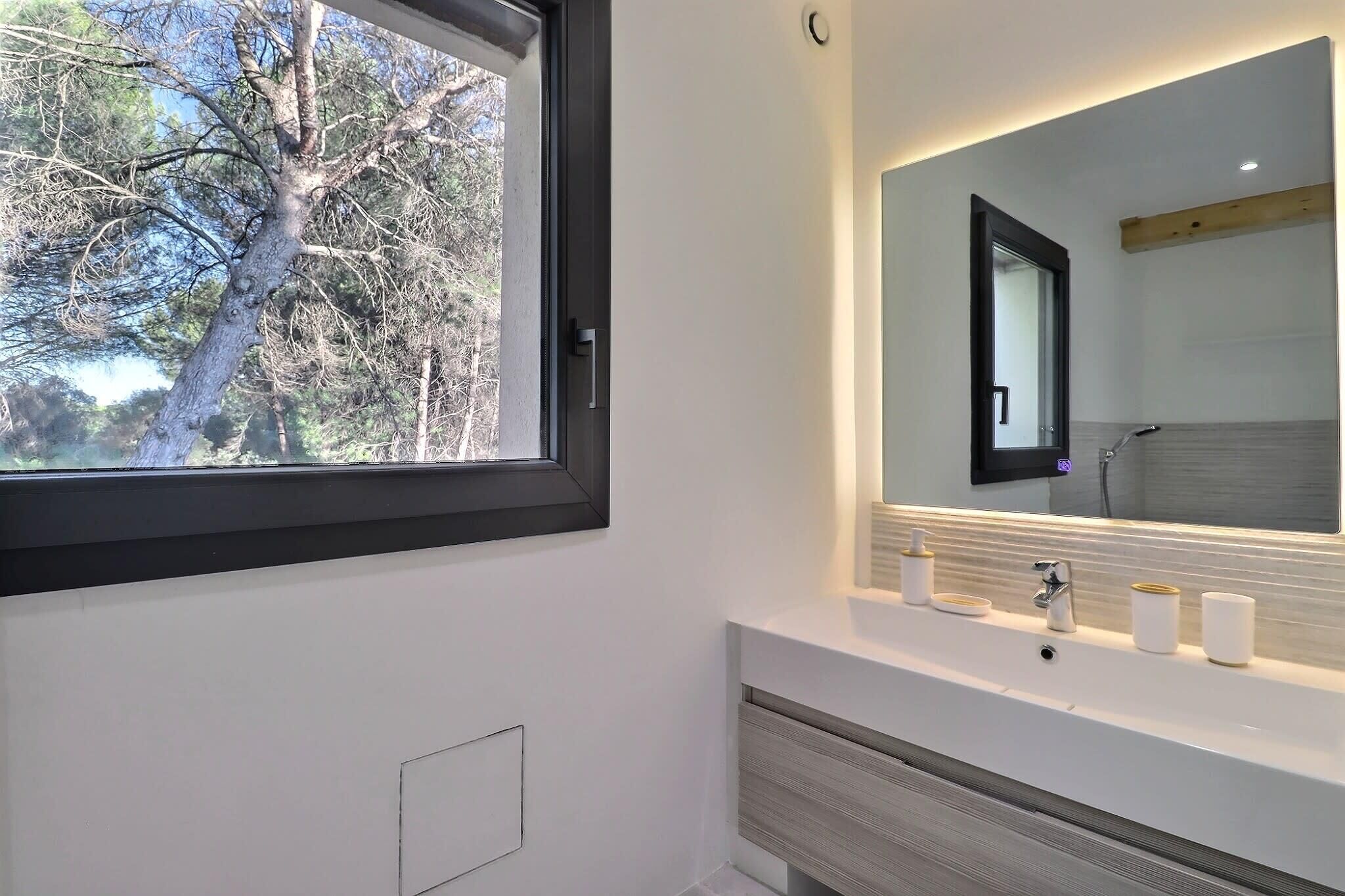 Une salle de bain moderne dotée d’une grande fenêtre, d’un lavabo intégré et d’un miroir.