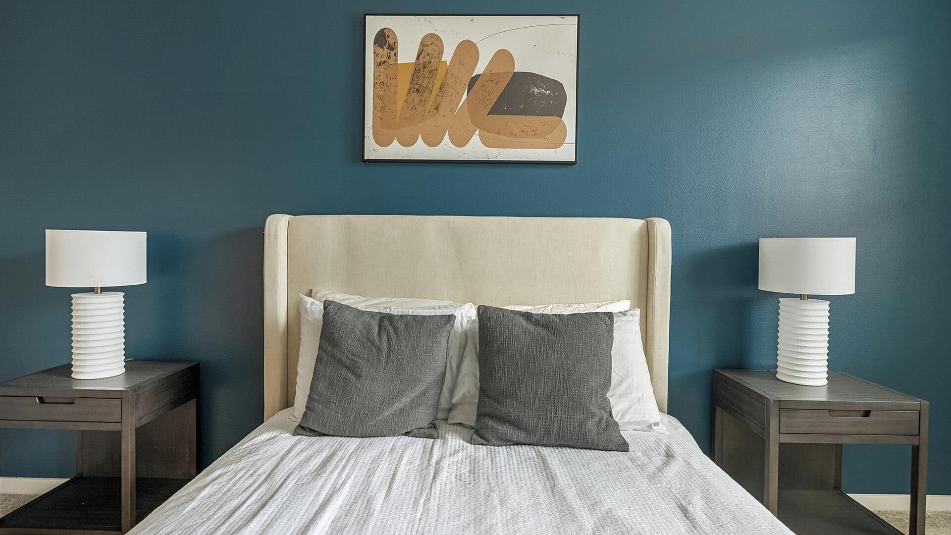 Una cama bien hecha con dos almohadas, un cabecero y dos mesitas de noche con lámparas.