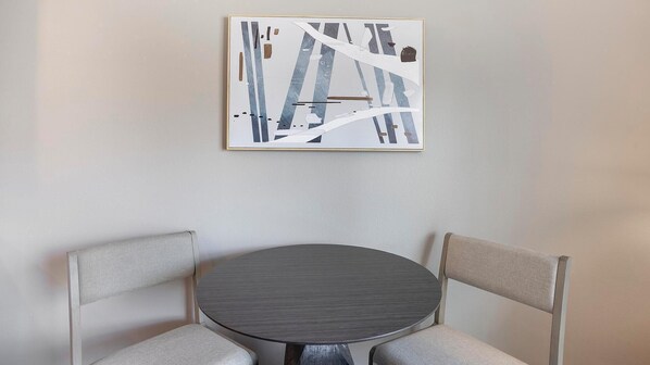 Una mesa redonda con dos sillas, una obra de arte abstracta enmarcada en la pared y una pared lisa.