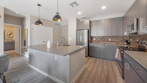 A modern kitchen with a large island, stainless steel appliances, and pendant lighting. - Landing | Stylish 1BD, Gym, Game Room (Phoenix)