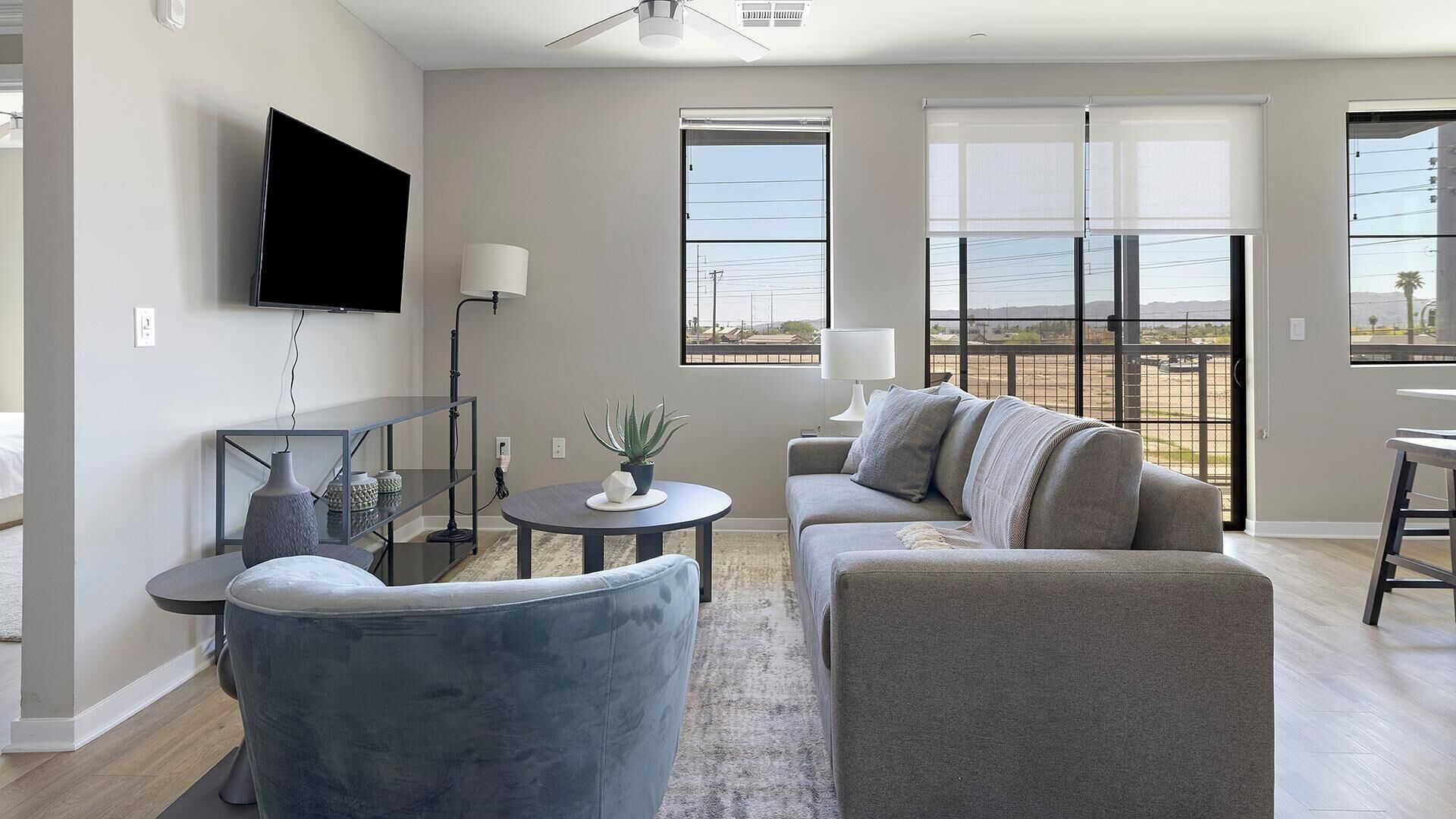 A modern living room with a flat-screen TV, a sofa, a coffee table, and a view of the outdoors through large windows.