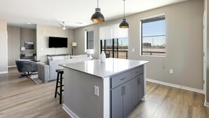 A modern kitchen with a central island, large windows, and a flat-screen TV.