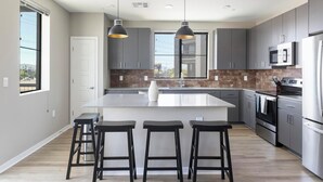 A modern kitchen with a central island, bar stools, stainless steel appliances, and a view of the outside.
