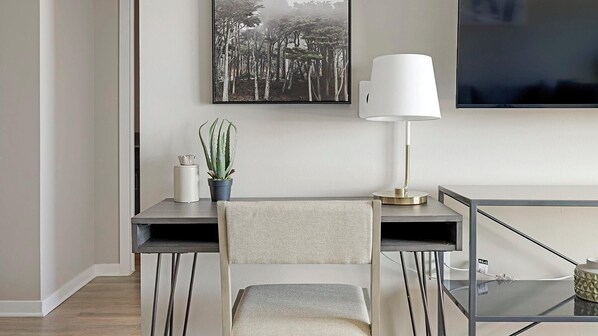Una sala de estar moderna con un escritorio, una silla, una planta en maceta, una lámpara y un televisor de pantalla plana montado en la pared.