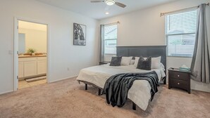 Une chambre à coucher avec un lit, une table de chevet, un ventilateur de plafond et une fenêtre avec des rideaux.