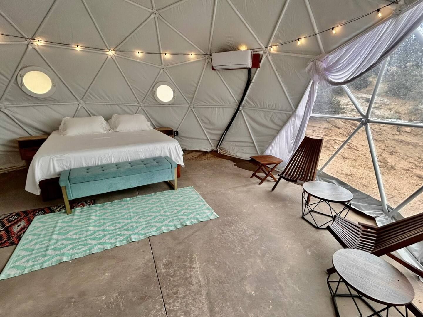 A tented accommodation with a bed, bench, table, and chairs.