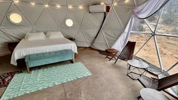 A tented accommodation with a bed, bench, table, and chairs.