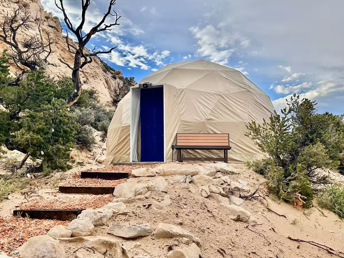 A dome-shaped tent with a blue door, surrounded by rocky terrain and sparse vegetation.