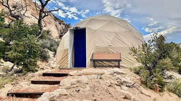 A dome-shaped tent with a blue door, surrounded by rocky terrain and sparse vegetation.