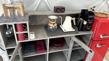 A compact kitchenette with a coffee maker, kettle, and storage for mugs and utensils.