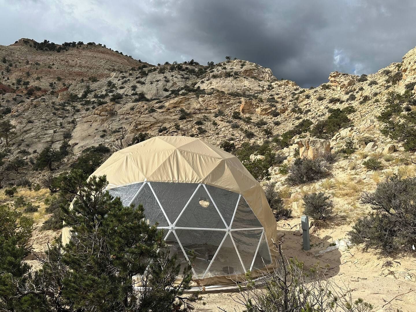 Uma tenda em formato de cúpula geodésica em uma paisagem desértica com colinas rochosas ao fundo.
