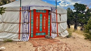 A traditional yurt with a red door and decorative patterns, set in a natural landscape with trees and a clear sky. - Roadside Mongolian Yurt (Teasdale)