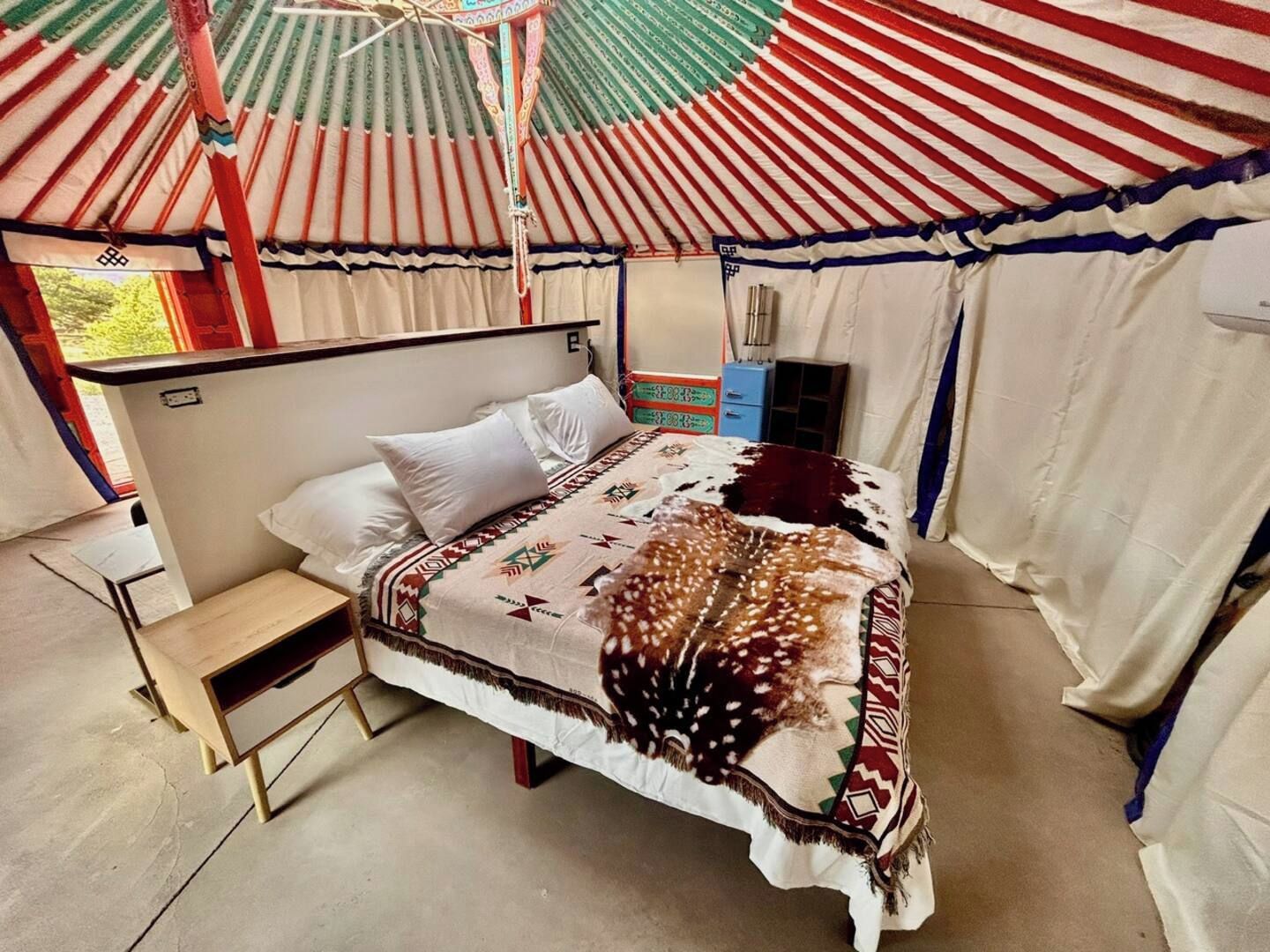 A single bed with a patterned blanket, a small bedside table, and a window with curtains.