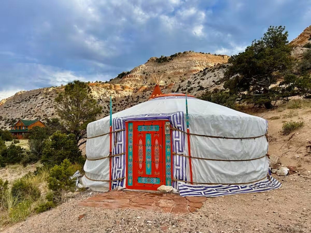 A traditional yurt with a red door, surrounded by a mountainous landscape.
