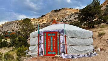 A traditional yurt with a red door, surrounded by a mountainous landscape.