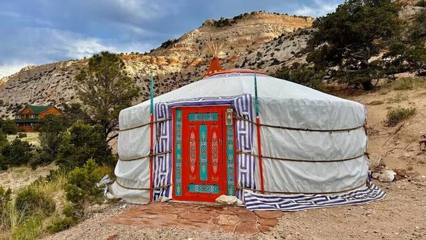 A traditional yurt with a red door, set against a mountainous backdrop. - Roadside Mongolian Yurt (Teasdale)
