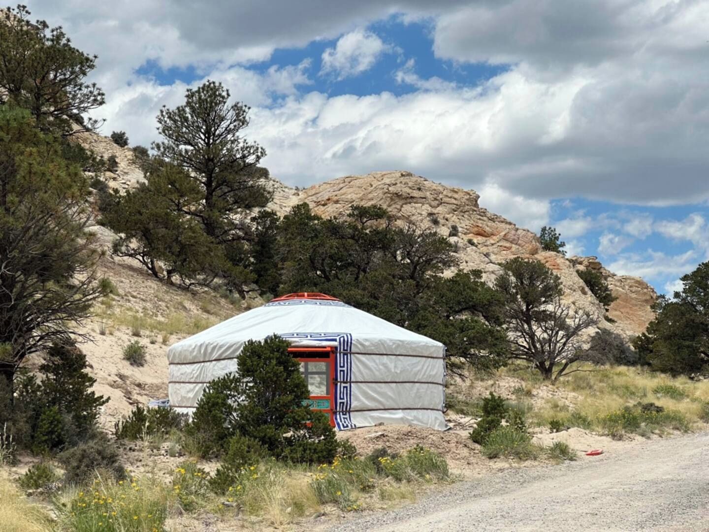 Een traditionele yurt met een rode deur, omgeven door woestijnvegetatie en een rotsachtige heuvel op de achtergrond.