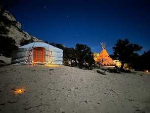 Une yourte avec une porte rouge et une structure conique illuminée, se détachant sur le ciel nocturne.