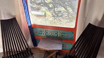 A room with two wooden lounge chairs, a small table, and a window with a view of trees.