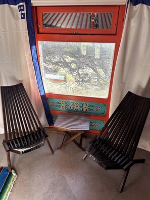 A room with two wooden lounge chairs, a small table, and a window with a view of trees. - Hilltop Yurt near Capitol Reef, King Bed (Teasdale)
