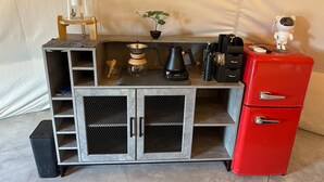 Una kitchenette con cafetera, un refrigerador rojo, una planta pequeña y una figura de juguete encima.