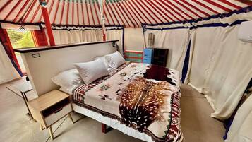 Una cama individual con una manta estampada, una mesita de noche pequeña y una ventana con cortinas.