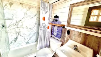 Ein Badezimmer mit einer Duschwand aus Marmor, einer weißen Toilette, einem weißen Waschbecken und einem Holz-Waschtisch.