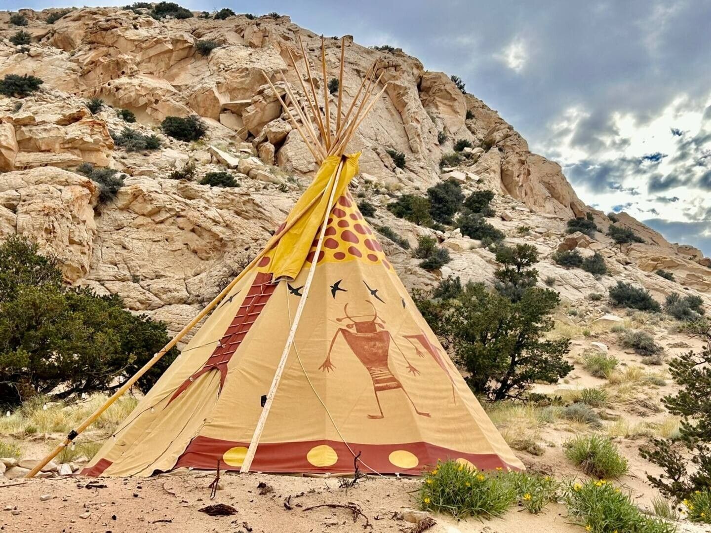A tipi with a painted design, set against a rocky desert landscape.